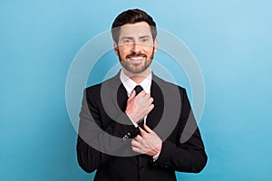 Photo of positive cheerful man manager wear black tuxedo fixing tie smiling isolated blue color background