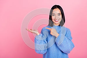 Photo of positive cute girl toothy smile indicate finger arm hold empty space  on pink color background