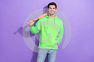 Photo of positive dangerous guy with brunet hairdo dressed green hoodie hold baseball bat on shoulder isolated on purple