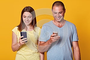 Photo of positive excited man and woman, looking at their smartphones screens with happy expressions, both using mobile phones