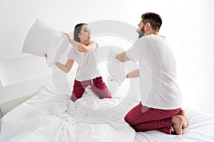 Photo of positive fooling husband wife nightwear fighting pillows indoors house bedroom photo