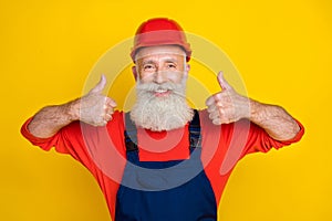 Photo of positive funky age man workwear overall red hard hat showing two thumbs up isolated yellow color background