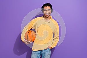 Photo of positive funky man wear yellow stylish clothes hold basketball ball have fun free time isolated on purple color