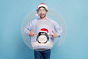 Photo of positive happy cheerful young man point finger sweater xmas penguin isolated on blue color background