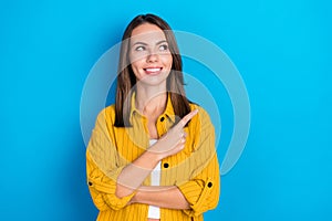 Photo of positive happy dreamy young woman look empty space point way ad isolated on blue color background