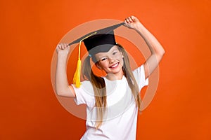 Photo of positive intelligent girl toothy smile arms touch mortarboard hat isolated on orange color background