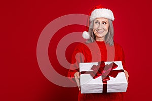 Photo of positive interested granny hold present package look copyspace wear hat pullover isolated red color background