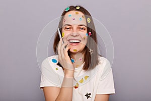 Photo of positive joyful beautiful woman covered with funny stickers holding smartphone and talking with friends, laughing