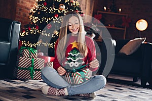 Photo of positive optimistic schoolgirl with blond hairstyle wear red sweater sit on floor opening gift box on new year