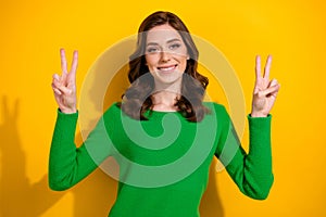 Photo of positive pretty girl toothy smile arms fingers demonstrate v-sign isolated on yellow color background