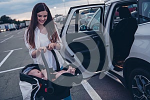 Photo of positive pretty mommy little son dressed casual clothes putting car seat inside auto transport open door