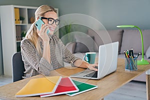 Photo of positive successful chief boss lady working remote netbook app talk colleagues smart phone in modern workspace