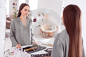 Photo of positive sweet lady grey sleepwear looking mirror applying make up indoors home bedroom