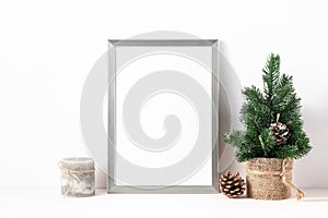 Photo or poster mockup with a silver frame, small decorative christmas tree  and candle