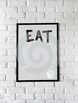 Photo of poster with text Eat in a black frame on a white brick wall. Empty space for text.