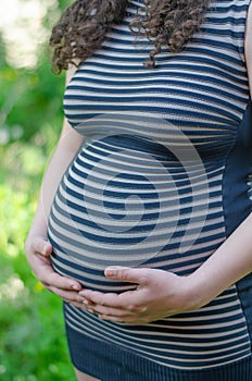 Photo of a pregnant girl in a striped dress with hands on her stomach