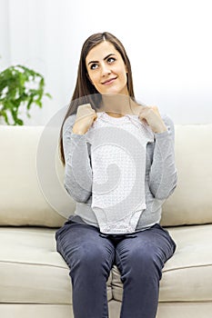 Photo of pregnant woman wearing casual clothes and holding childish clothes in hands.