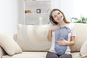 Photo of pregnant woman wearing casual clothes and holding childish clothes in hands.