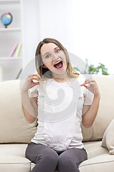 Photo of pregnant woman wearing casual clothes and holding childish clothes in hands.