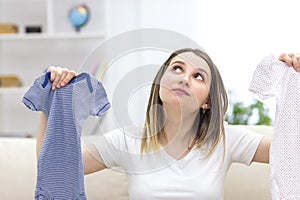 Photo of pregnant woman wearing casual clothes and holding childish clothes in hands.