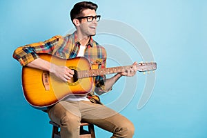 Photo of pretty adorable guy dressed plaid shirt spectacles smiling siting chair playing guitar empty space isolated