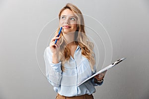 Photo of pretty blond secretary woman with long curly hair thinking and holding clipboard while working in office