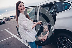 Photo of pretty charming mommy little son dressed casual clothes putting car seat inside auto transport open door