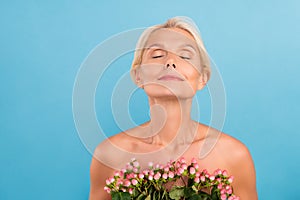 Photo of pretty charming senior woman nude shoulders closed eyes enjoying flowers aroma empty space isolated blue color