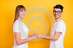 Photo of pretty cute young couple wear white t-shirt spectacles holding hands arms isolated yellow color background