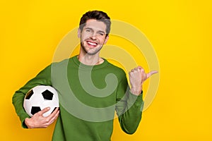 Photo of pretty cute young guy wear green sweater holding ball pointing empty space isolated yellow color background