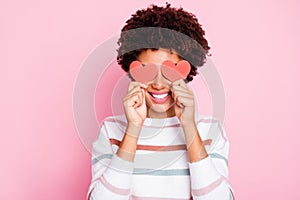 Photo of pretty dark curly skin lady holding in hands little red paper hearts hiding flirty eyes wear white striped