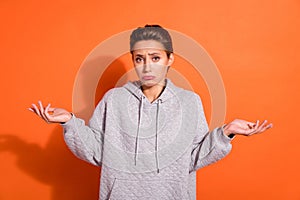 Photo of pretty doubtful young woman dressed grey hoodie shrugging shoulders isolated orange color background