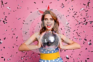 Photo of pretty excited lady hold glowing disco ball theme retro party dancing star confetti falling wear headband