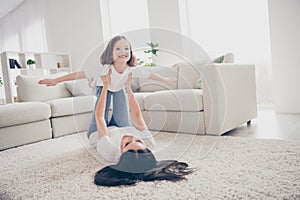 Photo of pretty funny little girl young mommy holding daughter hands above floor having fun pretending airplane flight