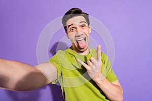 Photo of pretty funny young guy dressed green t-shirt smiling recoding video showing hard rock sign isolated purple