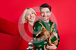 Photo of pretty funny young people wear ugly ornament pullovers holding dog recording video isolated red color