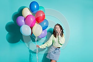 Photo of pretty girl hold bunch balloons arm cheekbone wear green pullover mini jeans skirt isolated blue color