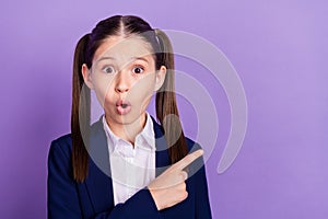 Photo of pretty impressed school girl wear blue uniform pointing finger empty space smiling isolated purple color