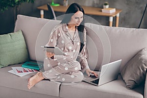 Photo of pretty optimistic girl sit write laptop hold tablet wear spectacles pijama at home on sofa photo