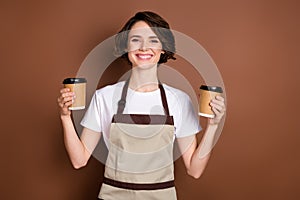 Photo of pretty positive girl toothy smile arms hold coffee cups look camera isolated on brown color background