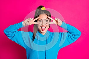 Photo of pretty positive person two hands fingers show v-sign near eye tongue out isolated on pink color background