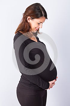 Photo of pretty pregnant woman keeping her hands on belly while looking at it