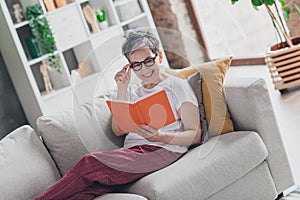 Photo of pretty retired woman read book sit sofa wear white outfit home flat rest relax spend free spare time living