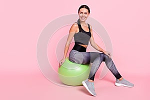Photo of pretty shiny young lady sportswear having rest big green fit ball smiling looking empty space isolated pink