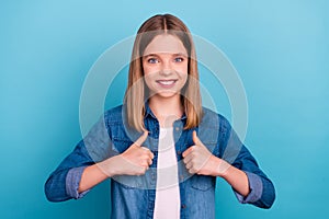 Photo of pretty teenager blond girl thumb up wear jeans shirt isolated on blue color background