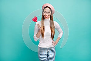 Photo of pretty traveler lady hold big candy on stick red heart figure toothy smiling good mood wear specs pink beret