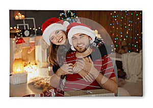 Photo printed on canvas. Happy young couple in Santa hats celebrating Christmas at home