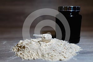 Photo of product spoon or measuring scoop of whey protein on black plastic jar background with lid on grey wooden background.