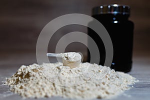 Photo of product spoon or measuring scoop of whey protein on black plastic jar background with lid on grey wooden background.