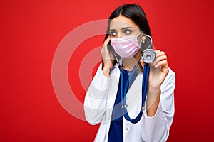 Photo of professional confident young european brunnet woman doctor in medical mask and white coat, stethoscope over